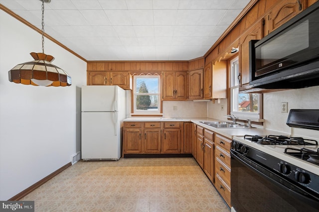 kitchen with brown cabinetry, freestanding refrigerator, gas stove, a sink, and black microwave