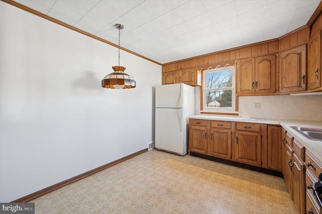 kitchen featuring crown molding, light countertops, freestanding refrigerator, and brown cabinets