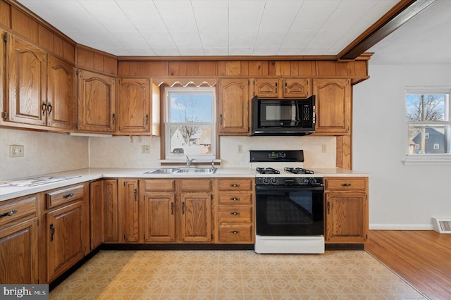 kitchen with brown cabinetry, black microwave, range with gas stovetop, and a sink