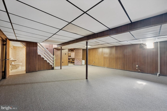 below grade area featuring stairway, wood walls, and a drop ceiling