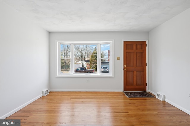 foyer with light wood finished floors, baseboards, and visible vents