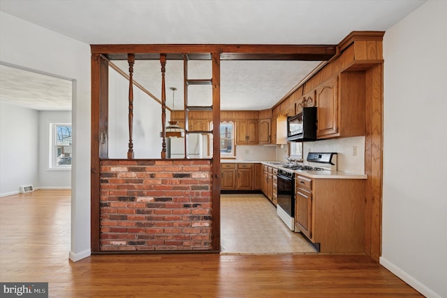 kitchen with black microwave, light countertops, light wood finished floors, and range with gas stovetop