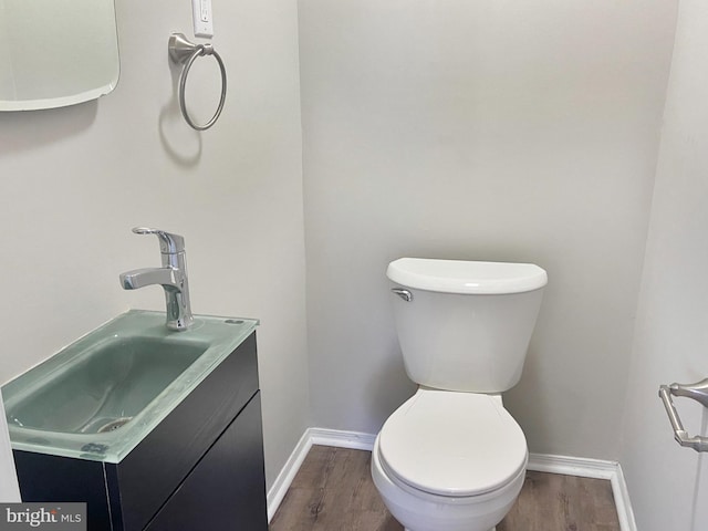 half bath with toilet, wood finished floors, vanity, and baseboards