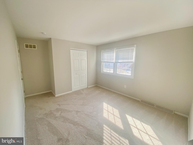 unfurnished bedroom with baseboards, visible vents, a closet, and light colored carpet