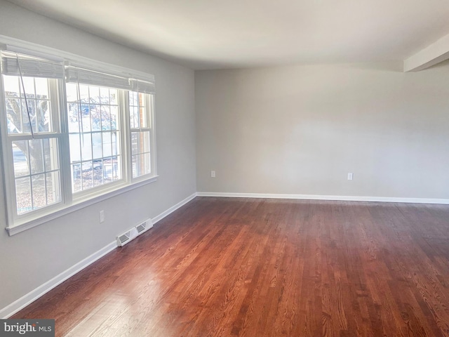 spare room featuring dark wood finished floors, visible vents, and baseboards