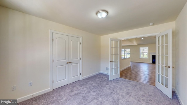 spare room with french doors, light carpet, a fireplace, and baseboards