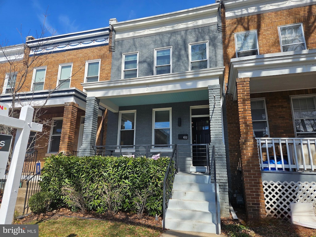 townhome / multi-family property featuring covered porch and brick siding