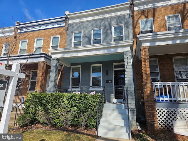 townhome / multi-family property featuring covered porch and brick siding