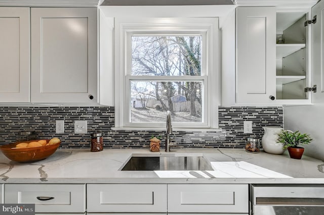 kitchen featuring glass insert cabinets, white cabinetry, a sink, and light stone countertops