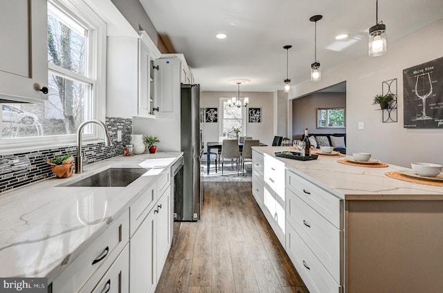 kitchen featuring light stone counters, a center island, pendant lighting, white cabinets, and a sink