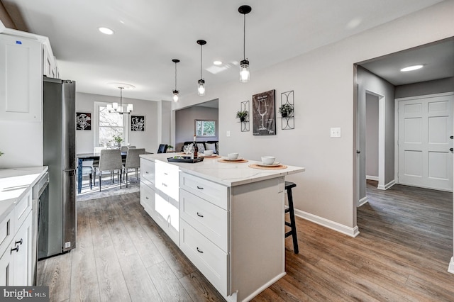 kitchen featuring a breakfast bar area, hanging light fixtures, white cabinetry, a kitchen island, and light stone countertops