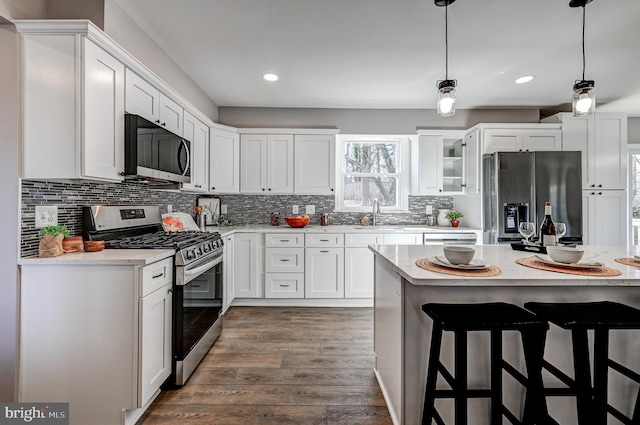 kitchen featuring stainless steel appliances, white cabinets, hanging light fixtures, light countertops, and glass insert cabinets