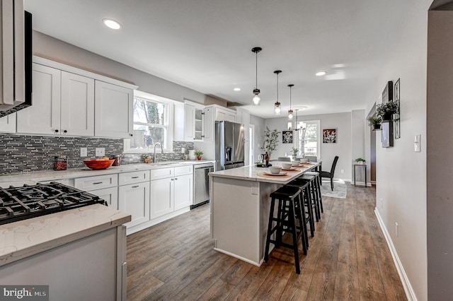 kitchen with stainless steel appliances, white cabinetry, a kitchen island, a sink, and a kitchen bar