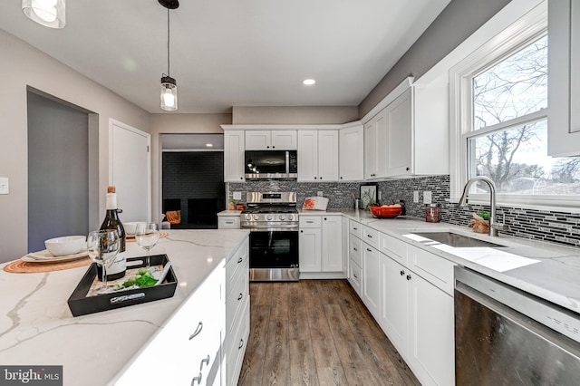 kitchen featuring appliances with stainless steel finishes, white cabinets, decorative light fixtures, and light stone countertops