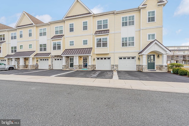 townhome / multi-family property featuring a standing seam roof, metal roof, a garage, stone siding, and driveway