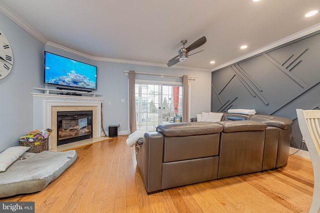 living room featuring ceiling fan, recessed lighting, a fireplace with flush hearth, ornamental molding, and light wood finished floors