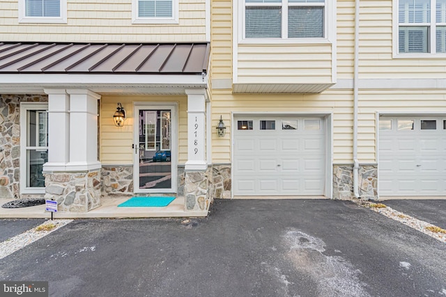 property entrance featuring stone siding, a standing seam roof, driveway, and a garage