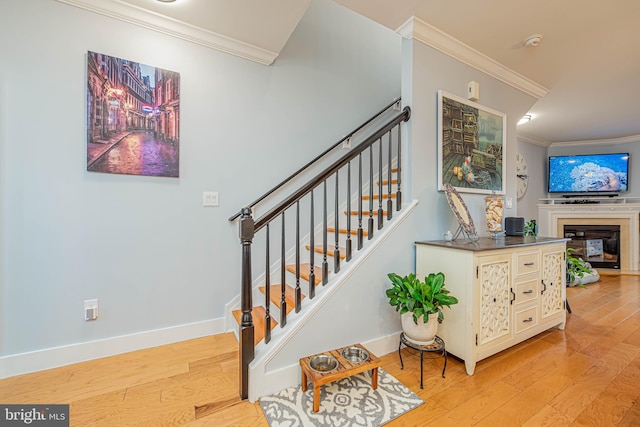 staircase featuring a glass covered fireplace, wood finished floors, and crown molding