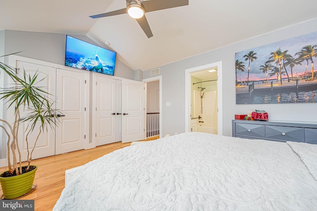 bedroom featuring light wood finished floors, two closets, lofted ceiling, visible vents, and ensuite bathroom