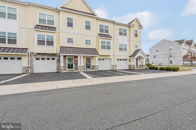 townhome / multi-family property featuring an attached garage, a standing seam roof, metal roof, stone siding, and driveway