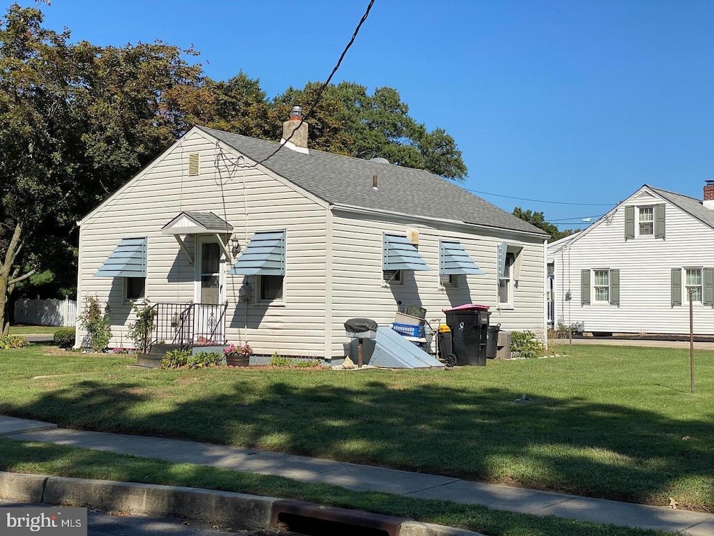 back of property with a shingled roof, a yard, and a chimney