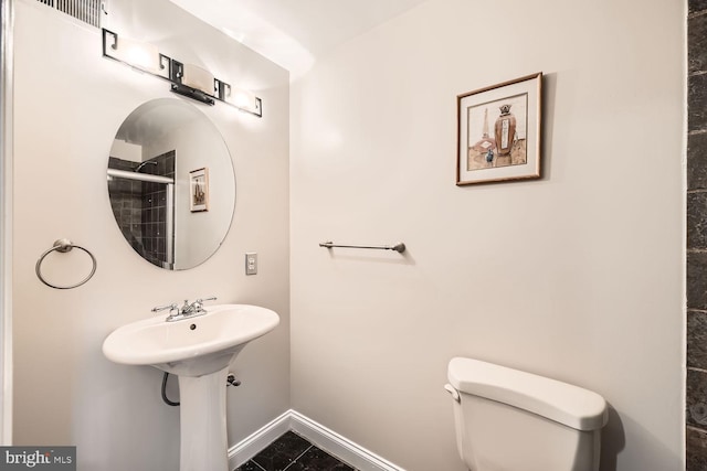 bathroom with toilet, a sink, baseboards, and tiled shower