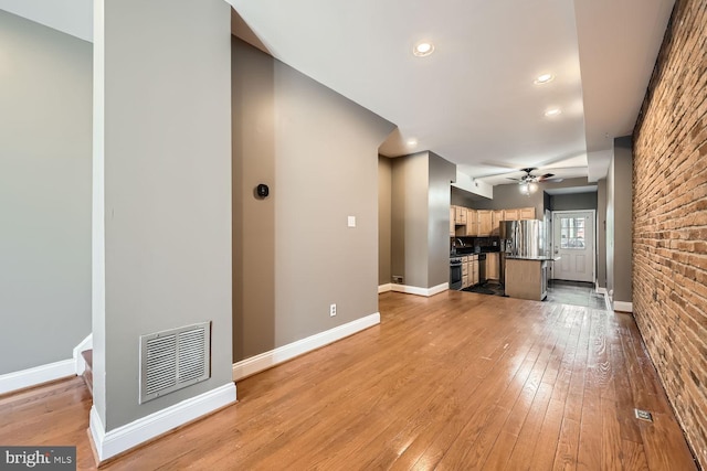 unfurnished living room featuring light wood-type flooring, baseboards, visible vents, and a ceiling fan