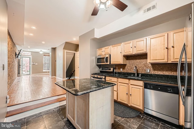 kitchen featuring visible vents, a kitchen island, dark stone countertops, stainless steel appliances, and a sink