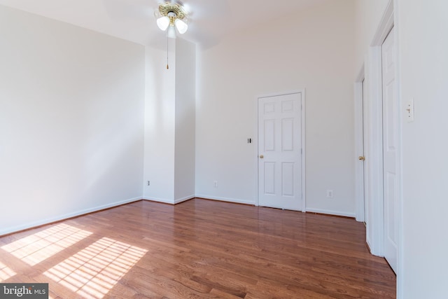 spare room with a towering ceiling, ceiling fan, baseboards, and wood finished floors