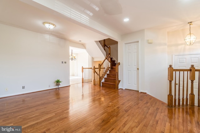 empty room with an inviting chandelier, stairs, baseboards, and wood finished floors