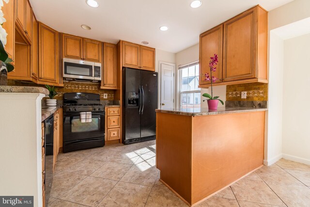 kitchen with brown cabinetry, a peninsula, black appliances, backsplash, and light tile patterned flooring