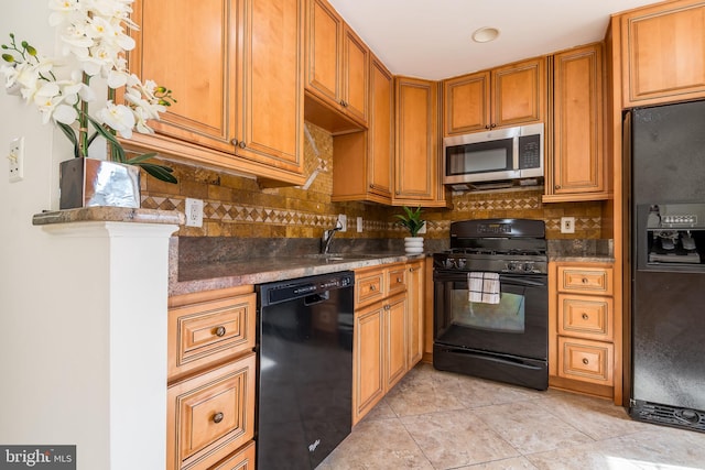 kitchen featuring a sink, decorative backsplash, black appliances, brown cabinetry, and dark countertops