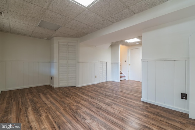 basement with a wainscoted wall, wood finished floors, and a paneled ceiling