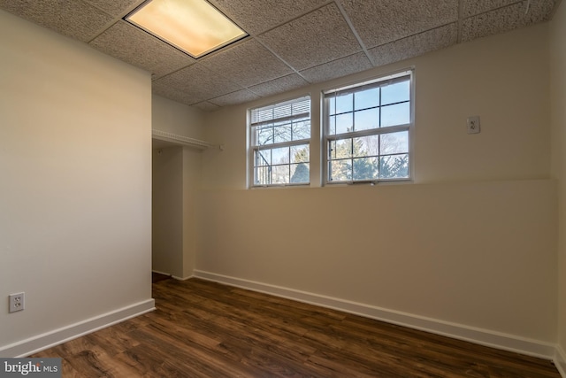 interior space with dark wood-style flooring, a drop ceiling, and baseboards