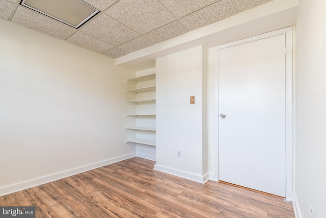 interior space with a closet, wood finished floors, a paneled ceiling, and baseboards