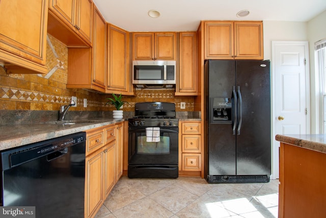 kitchen with tasteful backsplash, light tile patterned flooring, a sink, dark stone countertops, and black appliances