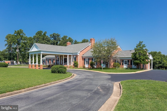 view of front facade with driveway, brick siding, a chimney, and a front yard