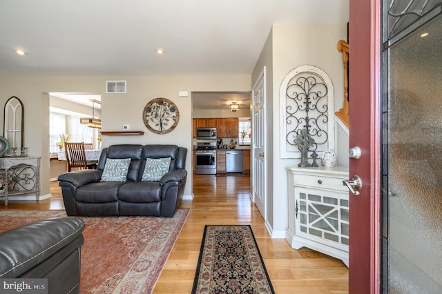 living area with light wood-type flooring, visible vents, and baseboards