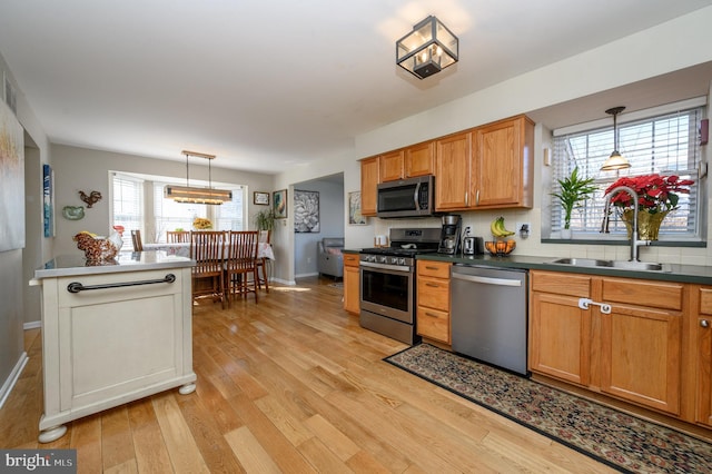 kitchen with brown cabinetry, appliances with stainless steel finishes, hanging light fixtures, light wood-type flooring, and a sink