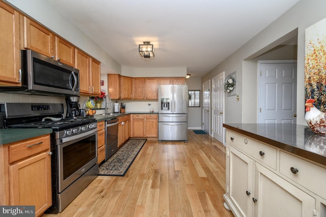 kitchen with light wood-style flooring, stainless steel appliances, a sink, decorative backsplash, and dark countertops