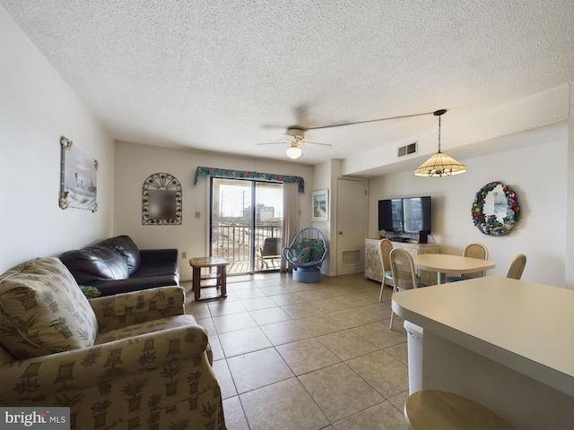 living area featuring a textured ceiling, light tile patterned flooring, visible vents, and a ceiling fan