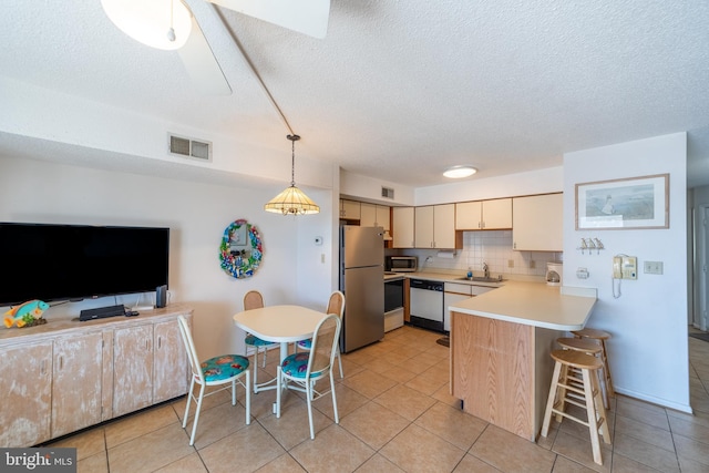 kitchen with a peninsula, visible vents, hanging light fixtures, appliances with stainless steel finishes, and light countertops