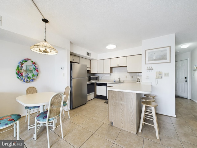 kitchen with pendant lighting, stainless steel appliances, light countertops, a sink, and a peninsula