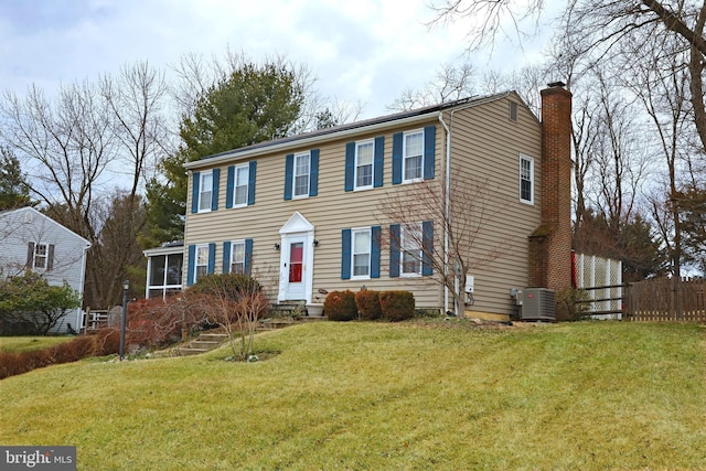 colonial home with central air condition unit, a chimney, a front lawn, and fence