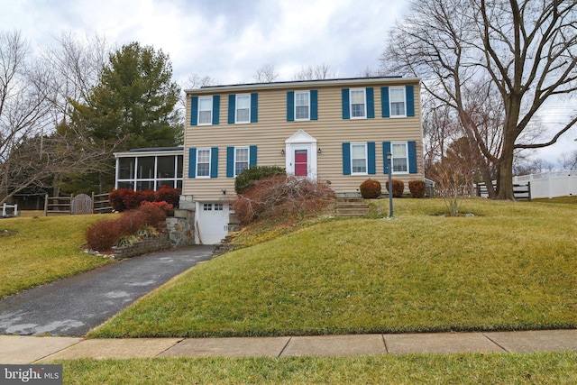 colonial inspired home with aphalt driveway, a garage, a front lawn, and a sunroom