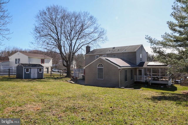 rear view of house with a fenced backyard, a shed, an outdoor structure, a sunroom, and a chimney