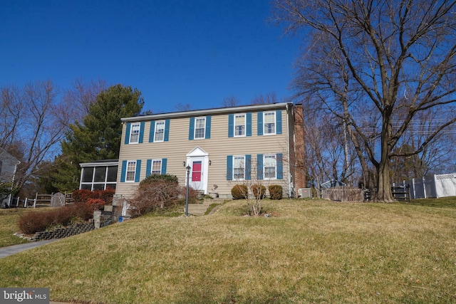 colonial-style house featuring a front lawn, fence, and a sunroom