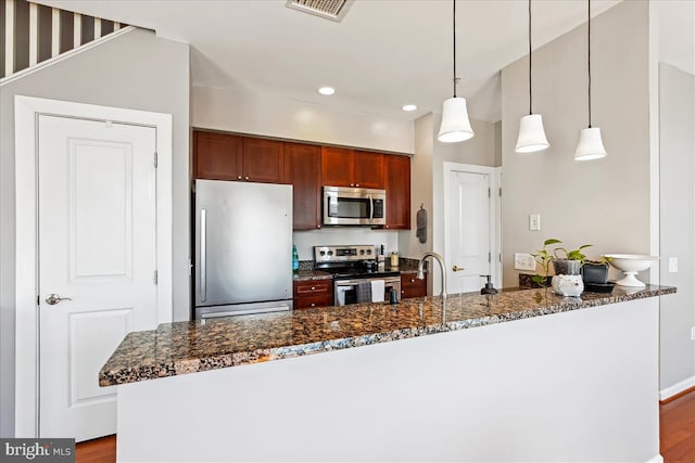 kitchen featuring visible vents, dark stone counters, appliances with stainless steel finishes, hanging light fixtures, and a sink