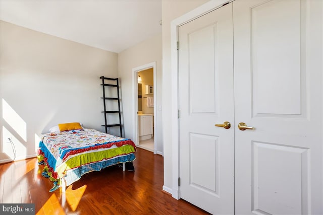 bedroom with ensuite bath, wood finished floors, and baseboards