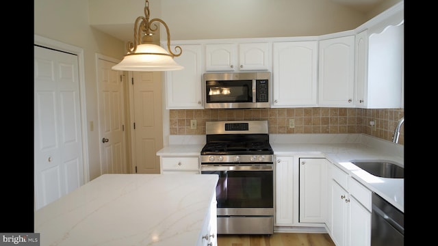 kitchen featuring appliances with stainless steel finishes, white cabinets, a sink, and decorative light fixtures